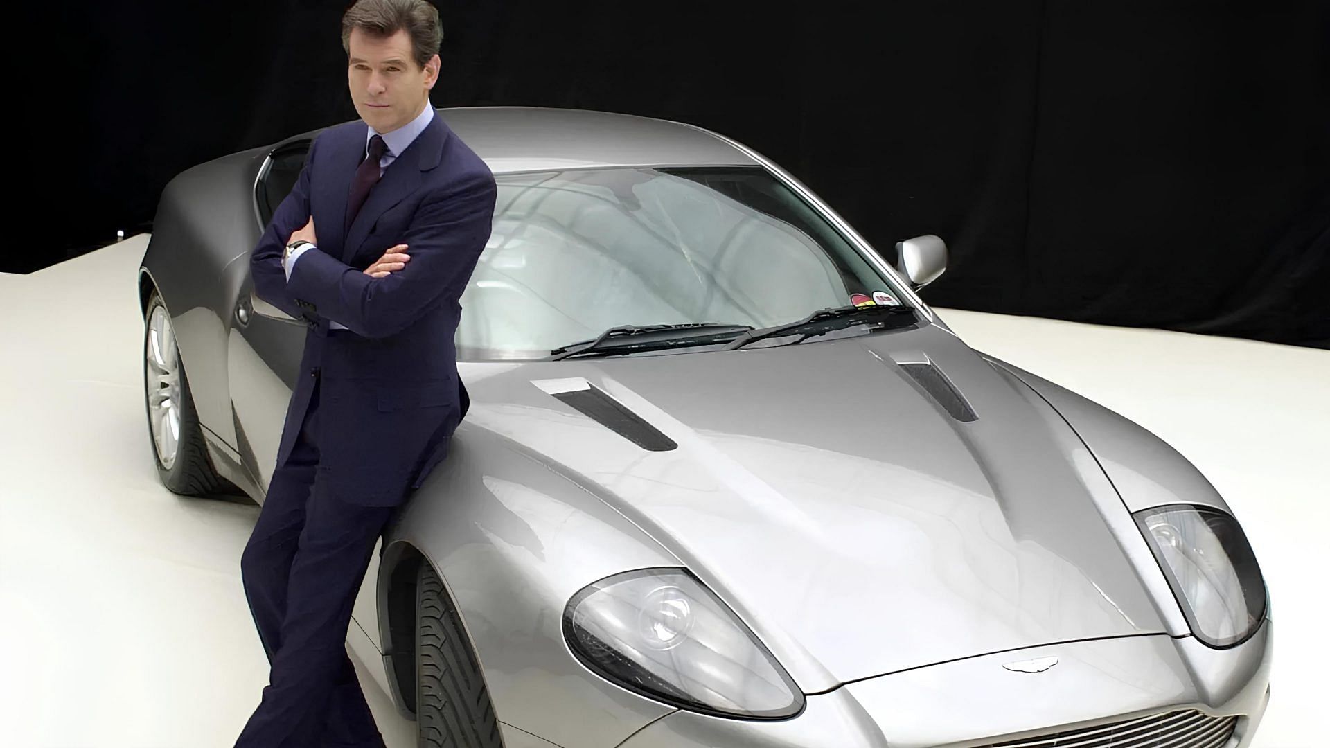 Pierce Brosnan standing beside a 2002 Aston Martin V12 Vanquish